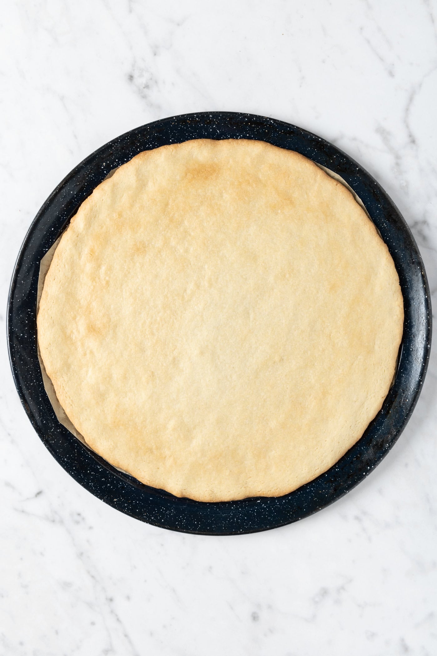Baked sugar cookie crust sitting on a round baking pan.