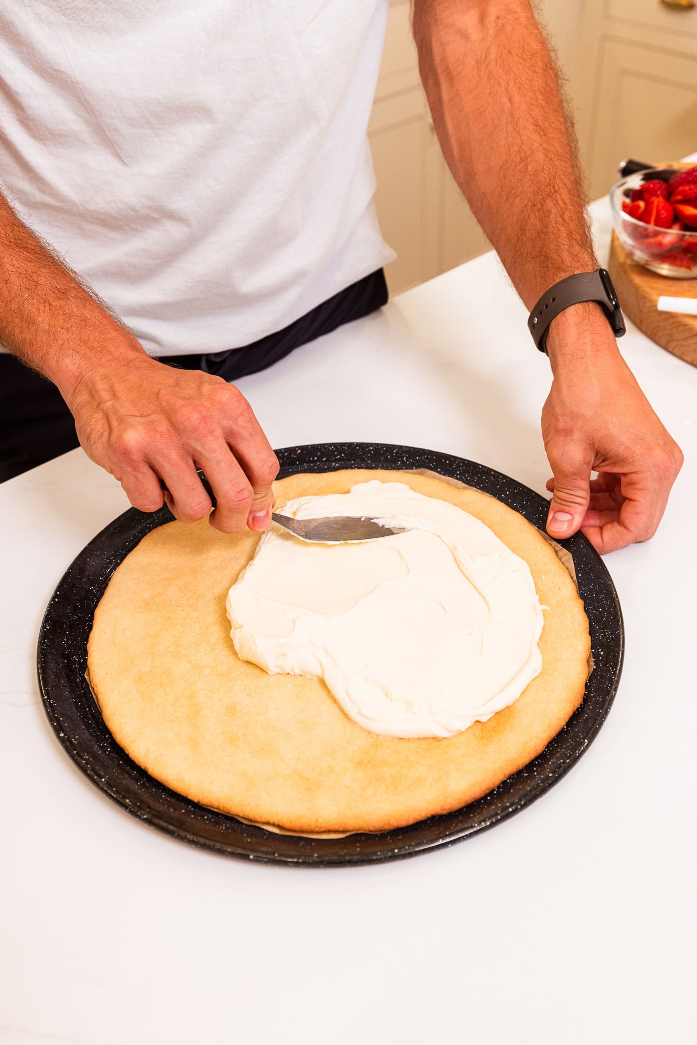 Hand using offset spatula to spread cream cheese frosting on top of a baked sugar cookie crust for a fruit pizza.