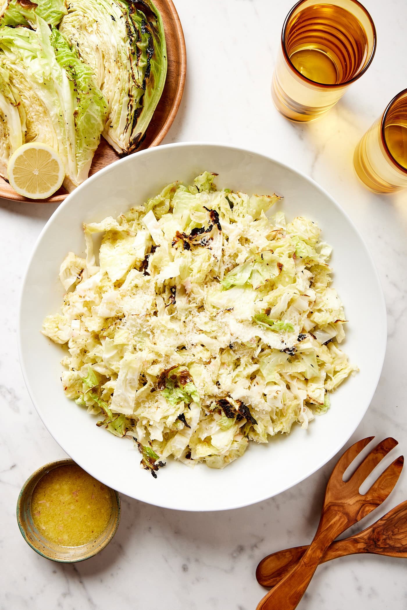 Large white bowl with chopped cabbage with charred edges and Parmesan cheese mixed together on white surface.