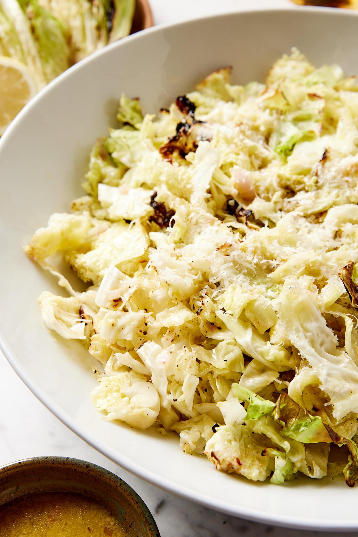 Large white bowl with grilled cabbage salad with grated Parmesan cheese on top showing charred edges.