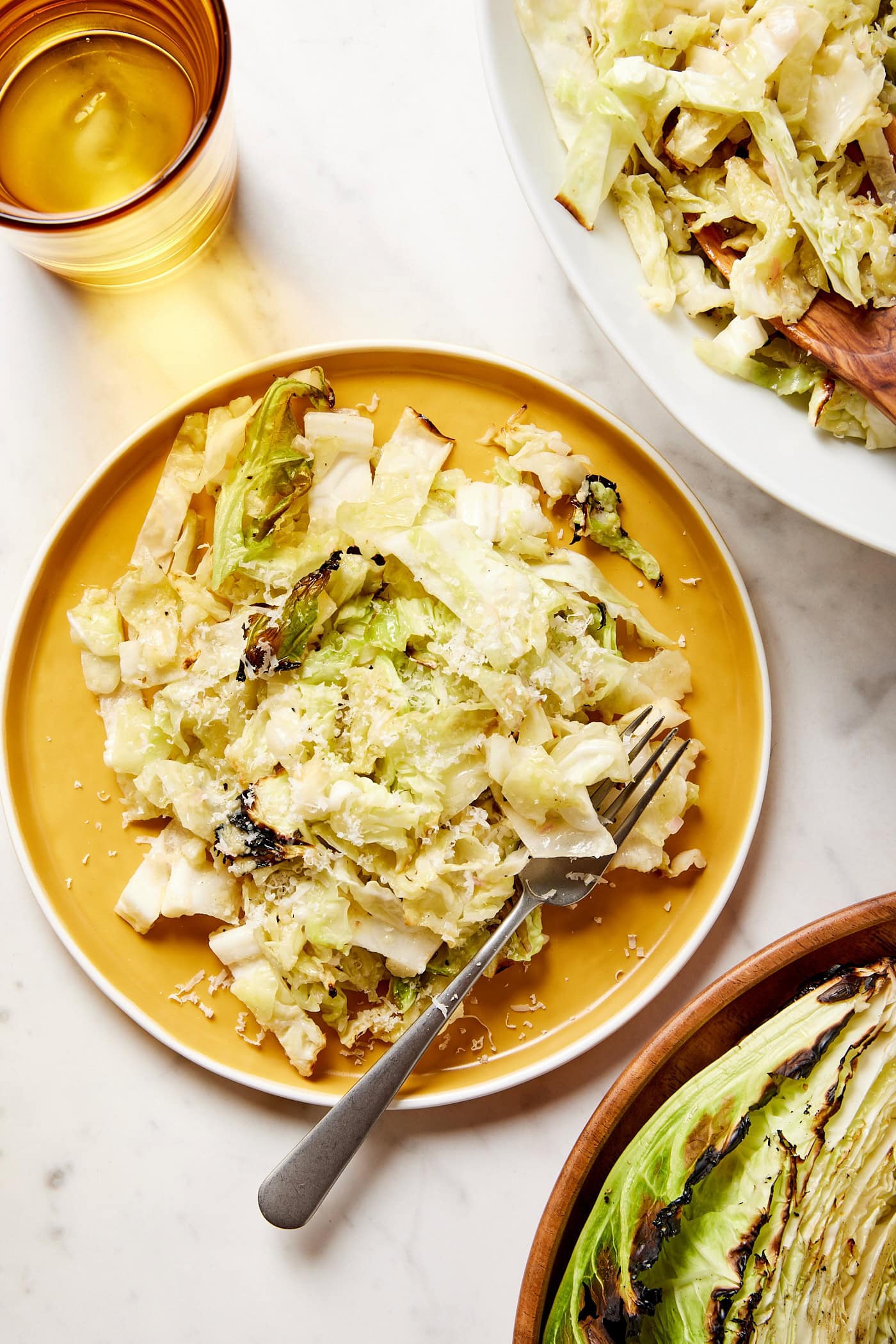 Yellow plate with serving of cabbage with charred edges with fork resting on plate and yellow glass to the side.