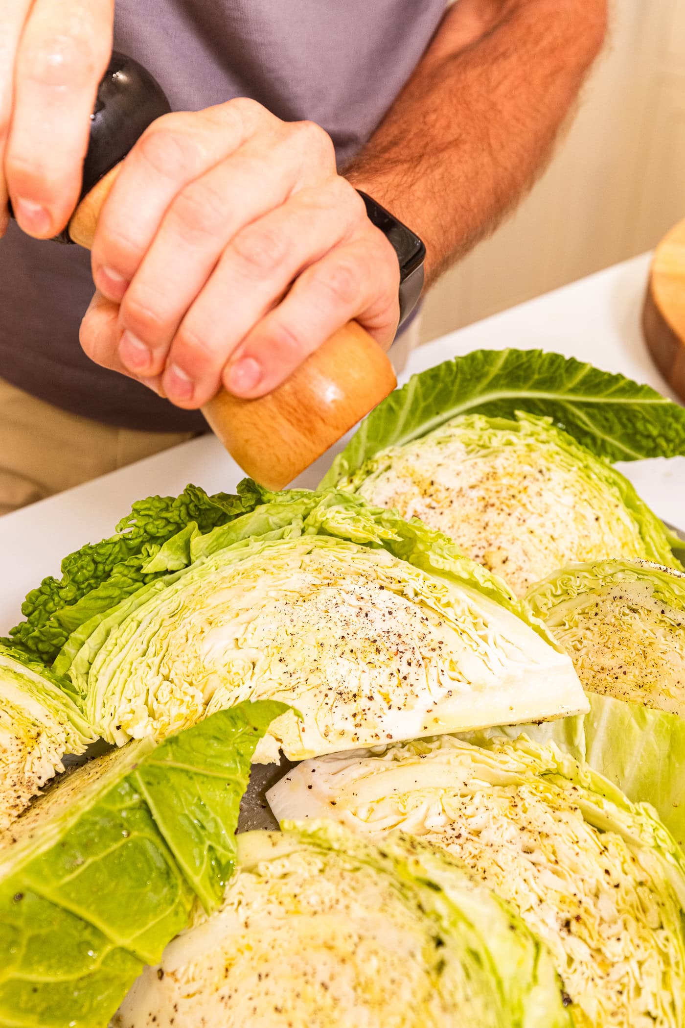 Black pepper being ground on top of wedges of cabbage before they're grilled.