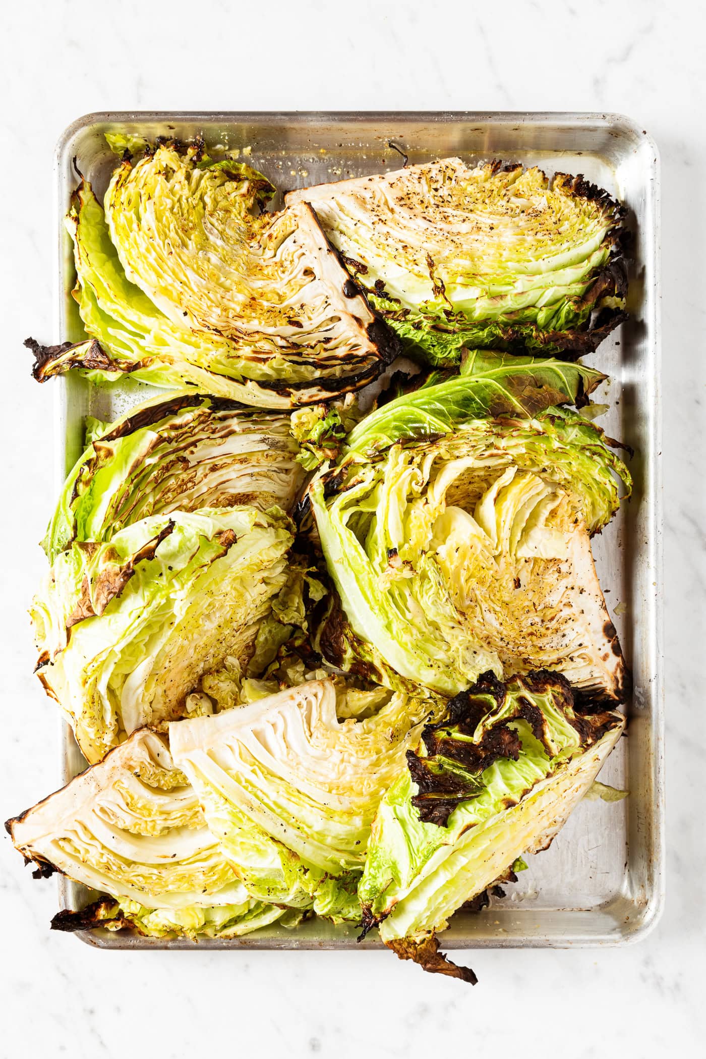 Metal baking pan filled with grilled cabbage showing char marks on edges.
