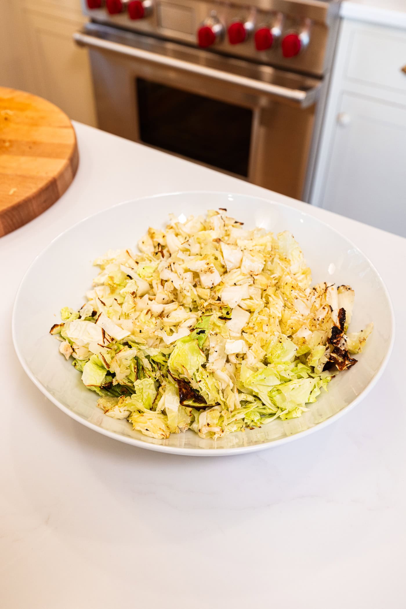 Chopped cabbage pieces with charred edges in a large white serving bowl on white surface.