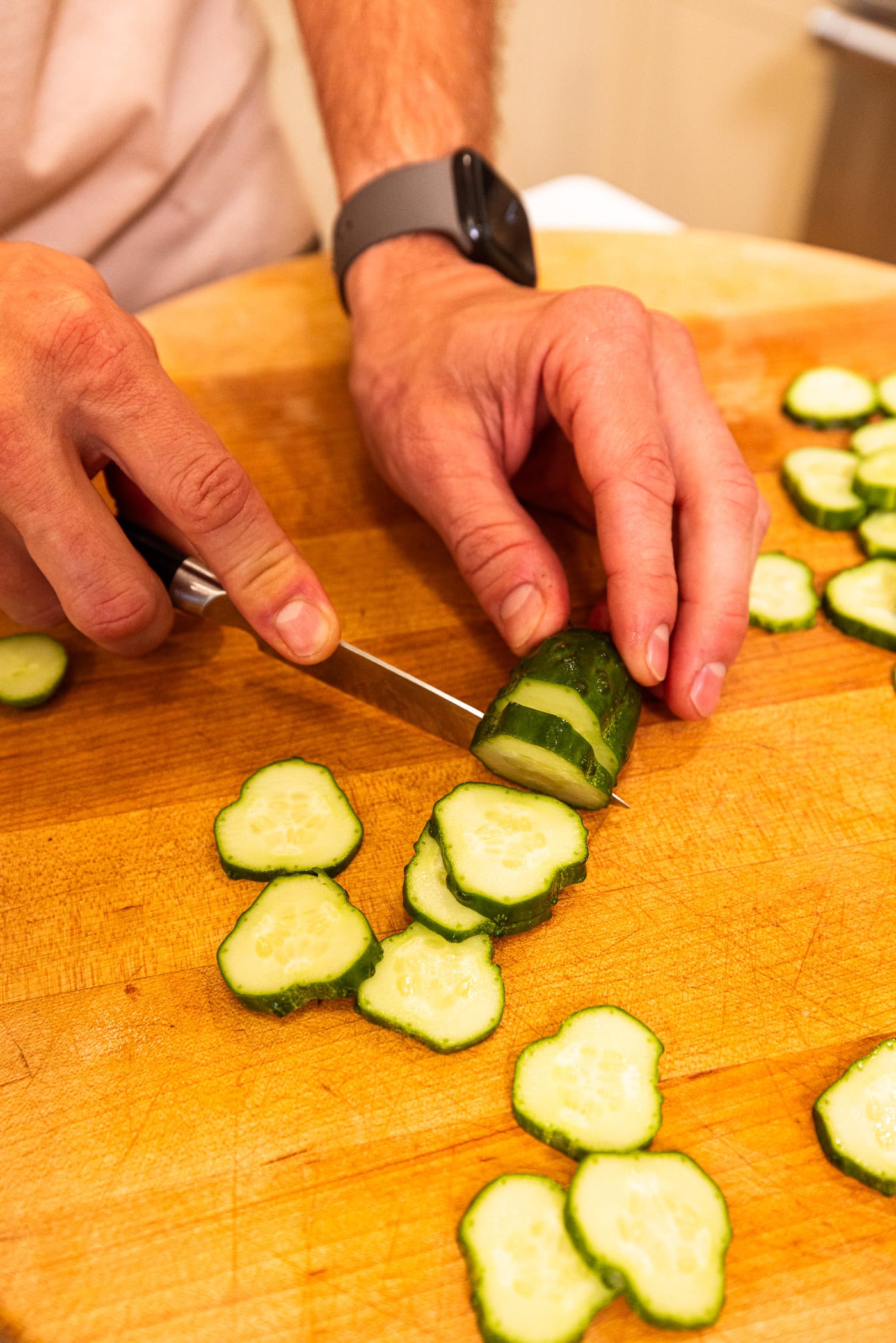 Hand using knife to slice cucumber into chips for dill pickles.