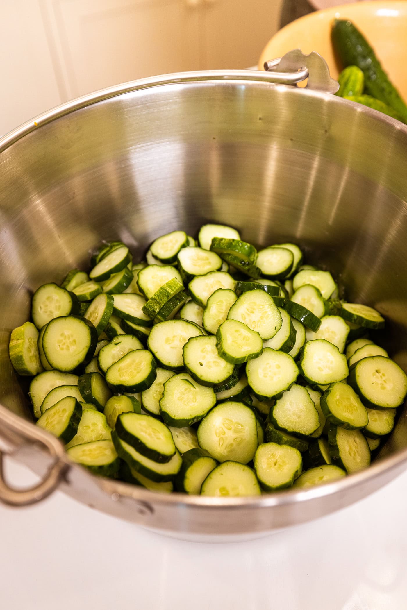Slices of cucumber ready to be canned with salt on them in a large metal kettle.