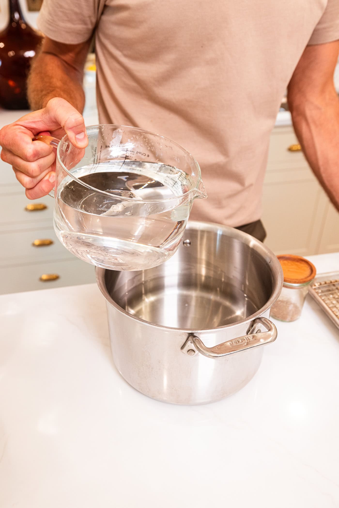 Hand pouring vinegar into a large metal pot filled with water for a pickle brine.