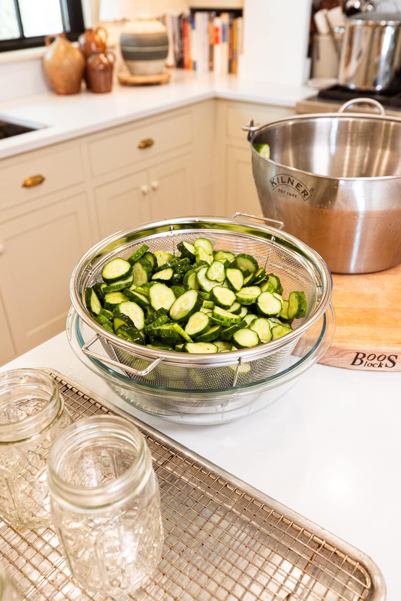 Slices of cucumber dripping their excess liquid in a strainer into a bowl.