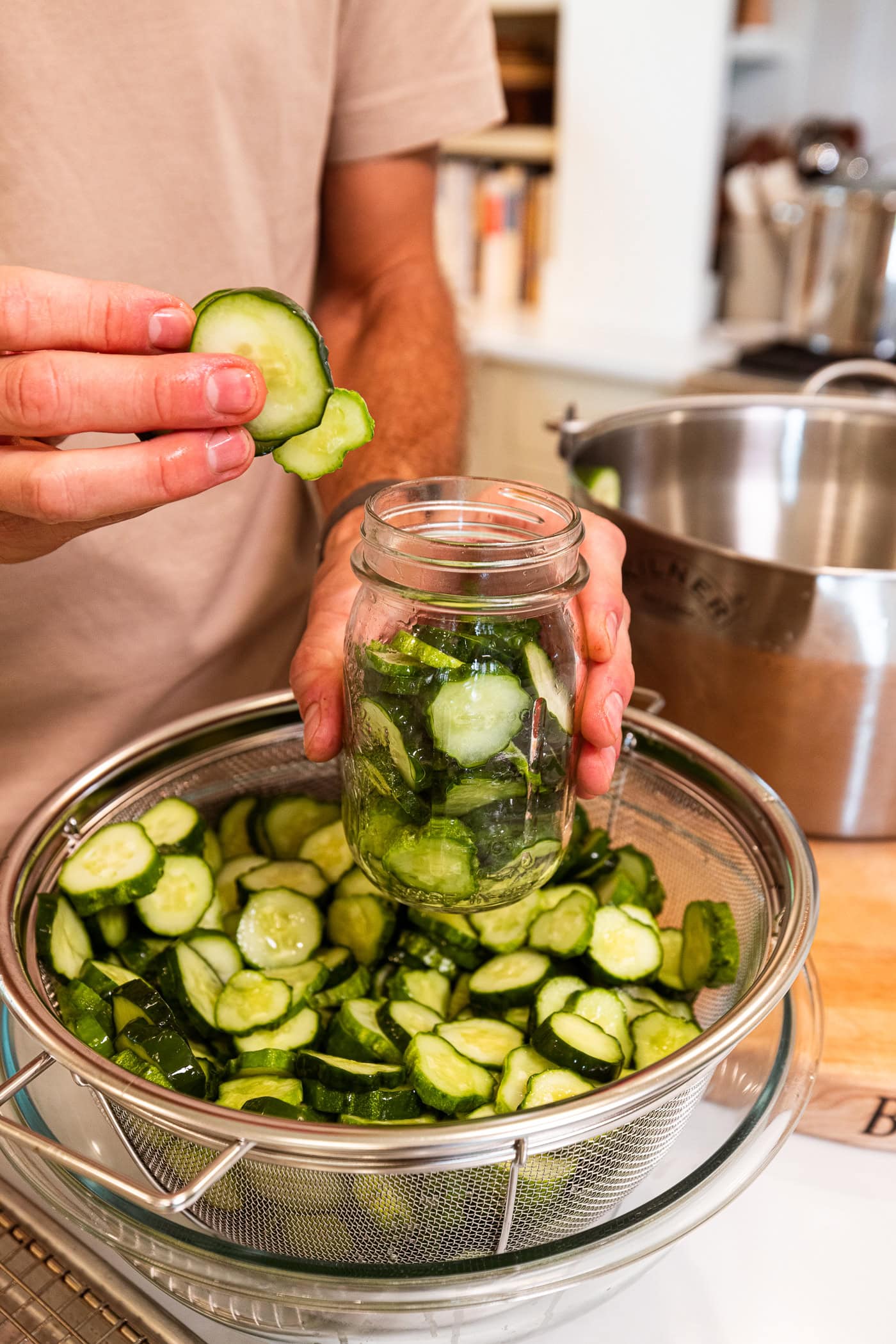 Hand placing slices of cucumber into a pint jar to make dill pickles.