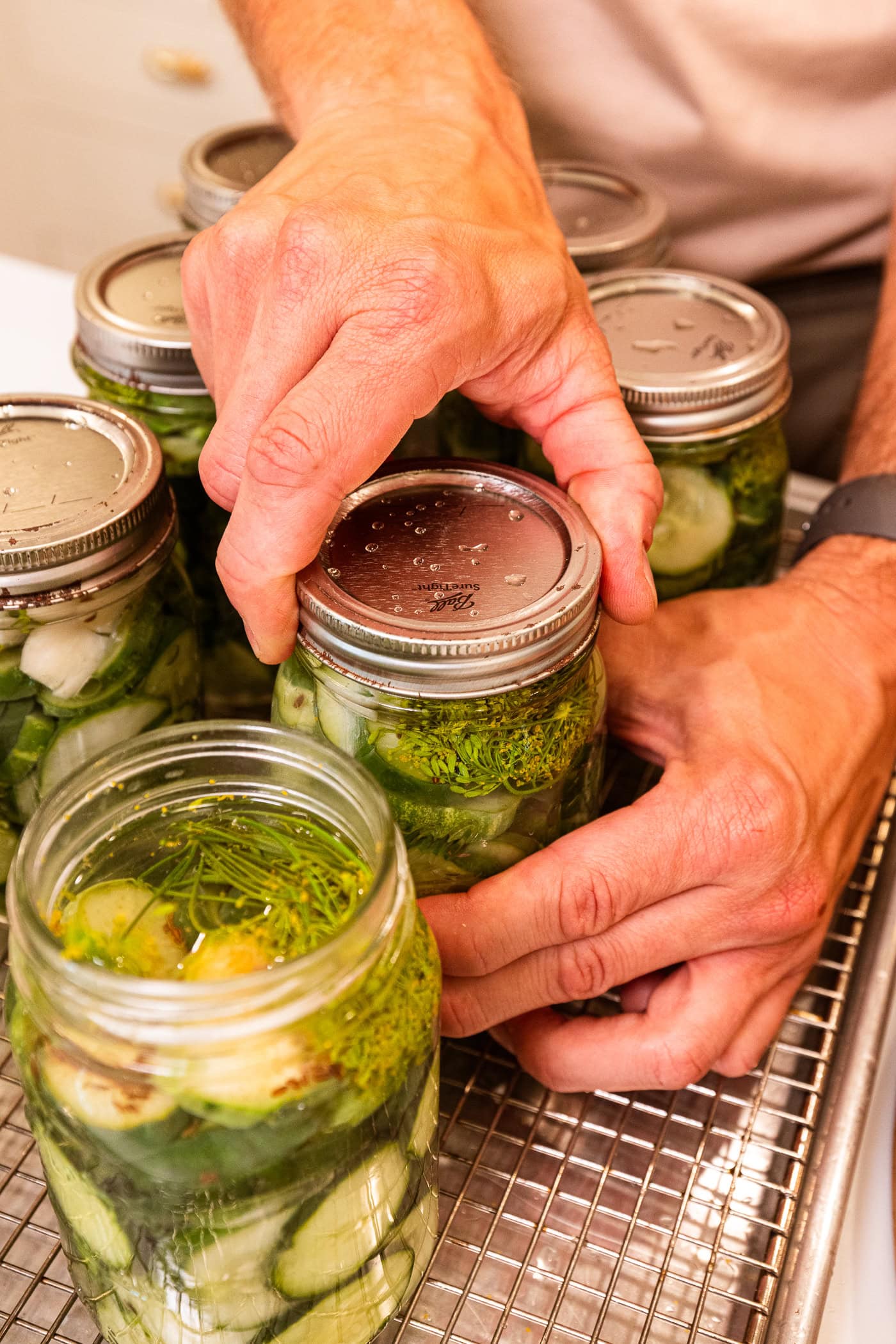 Hand tightening the lid and ring on a canning jar filled with pickles.