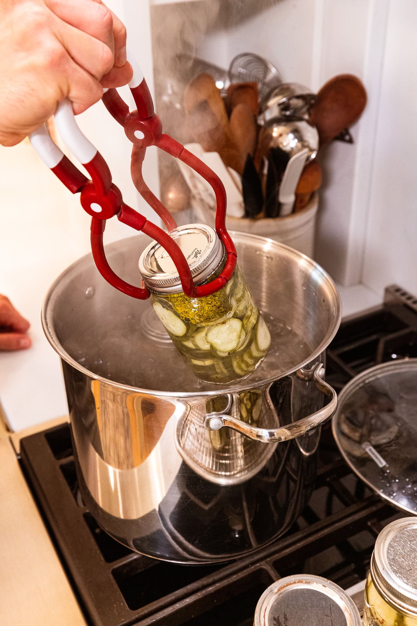Jar lifter lifting jars of canned dill pickles out of a water bath canner after being processed.