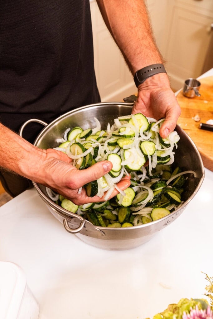 Mixing salt into a pot full of sliced cucumbers and onions.