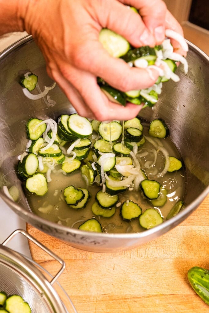 Pulling sliced cucumbers out of a large pot.