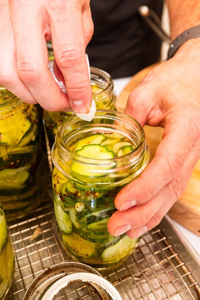 Wiping the rim of a pickle-filled jar with a paper towel.