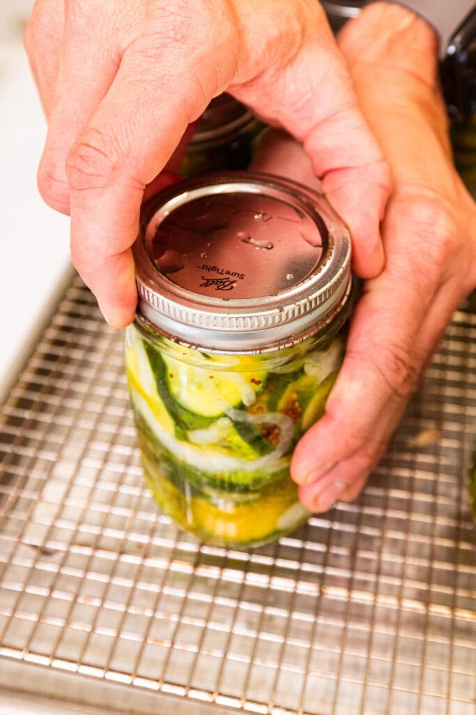 A hand tightening a ring down on a glass jar full of pickles.