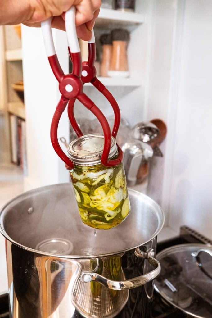 Lifting a jar of bread and butter pickles out of a boiling pot of water.