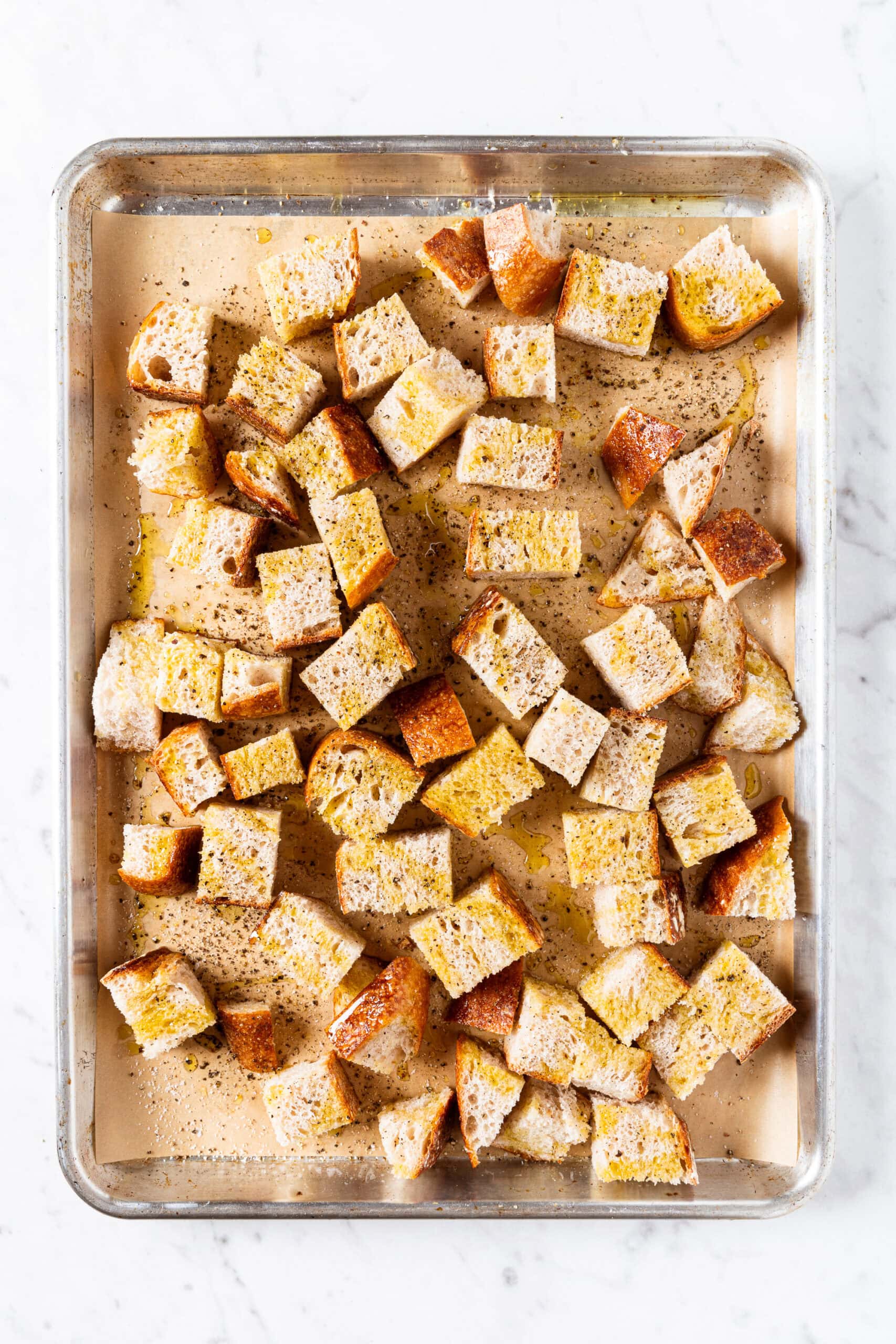 Sheet pan filled with bread cubes drizzled with olive oil, salt, and pepper before going into the oven.