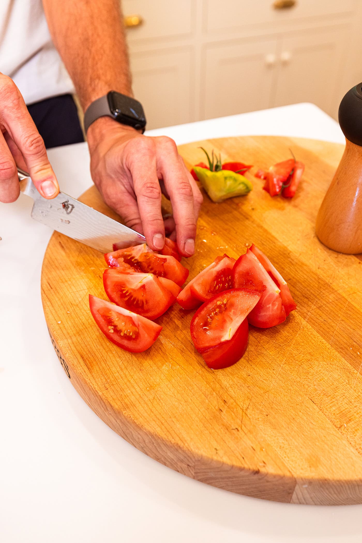 Hand using a knife to slice tomatoes into wedges on a wooden cutting board for a panzanella salad.