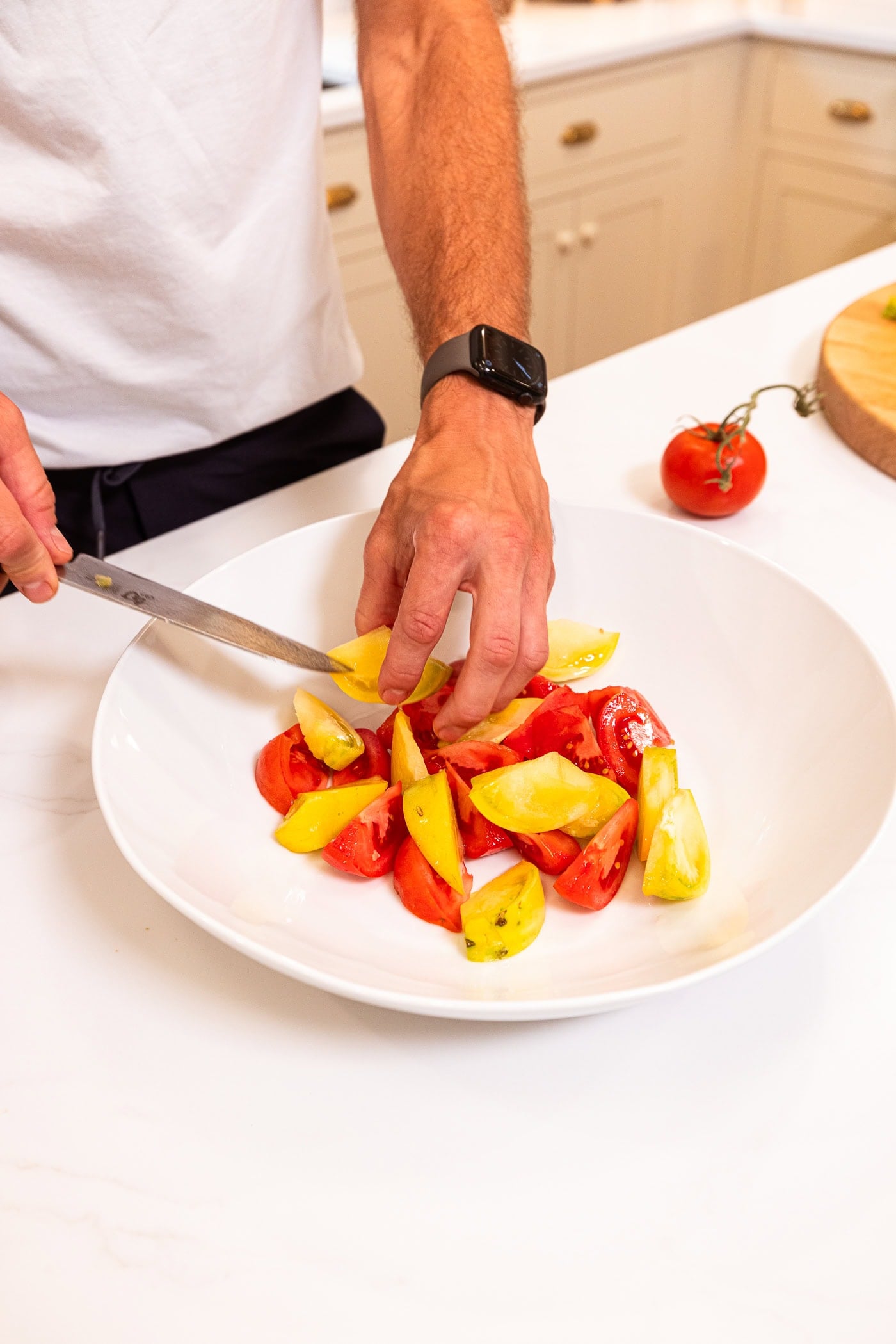 Hand holding red and yellow tomatoes and placing them into a large white bowl for a salad.