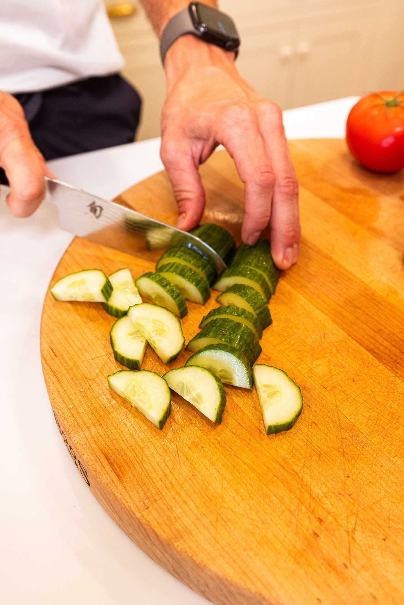 Hand slicing cucumbers into wedges on a wooden cutting board.