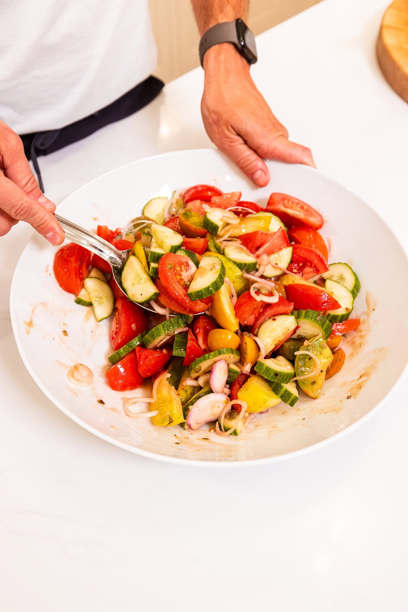 Large white bowl with hand tossing panzanella salad together with a large spoon.