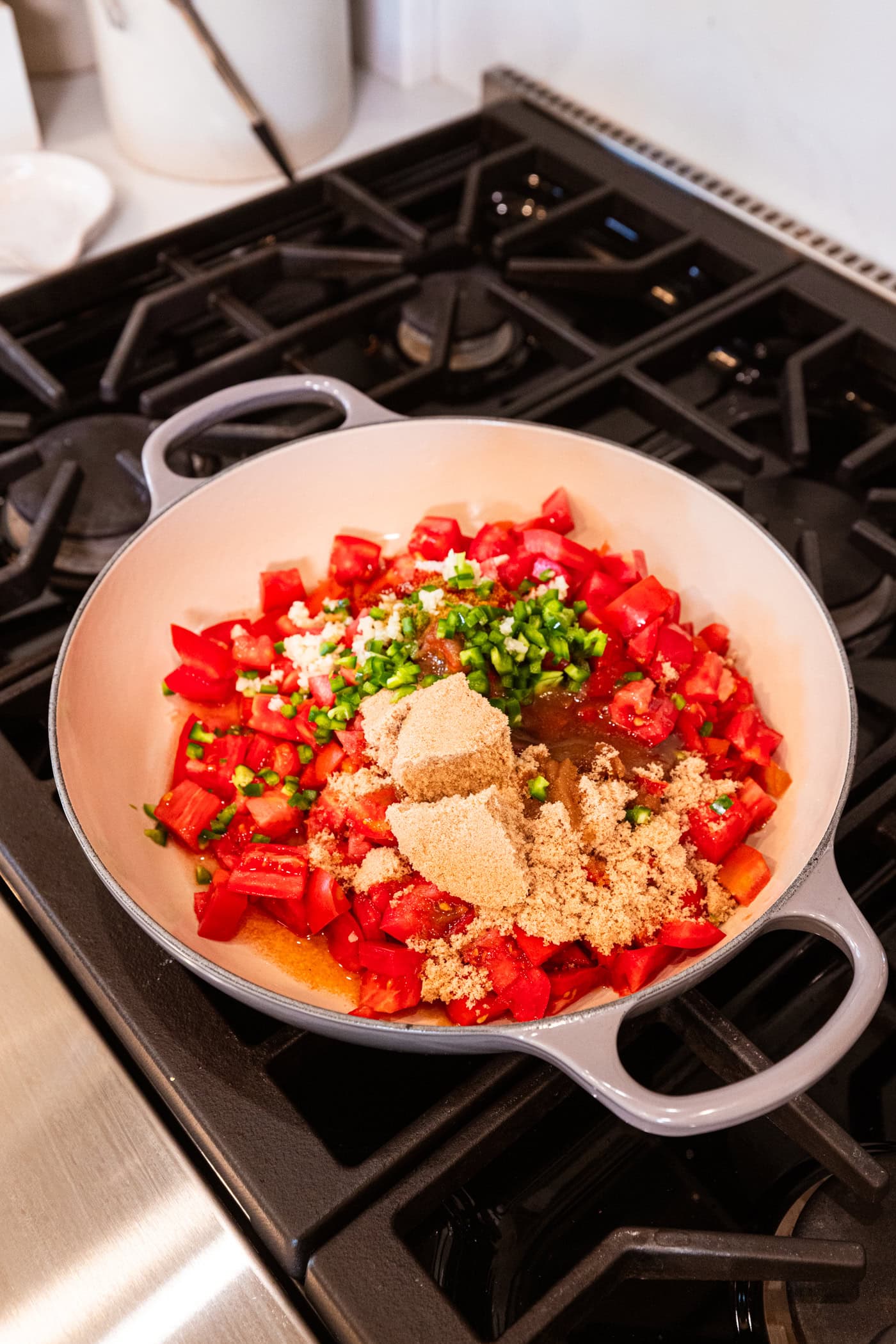 Large skillet filled with chopped tomatoes, jalapeño, brown sugar, and more spices all for tomato jam recipe.