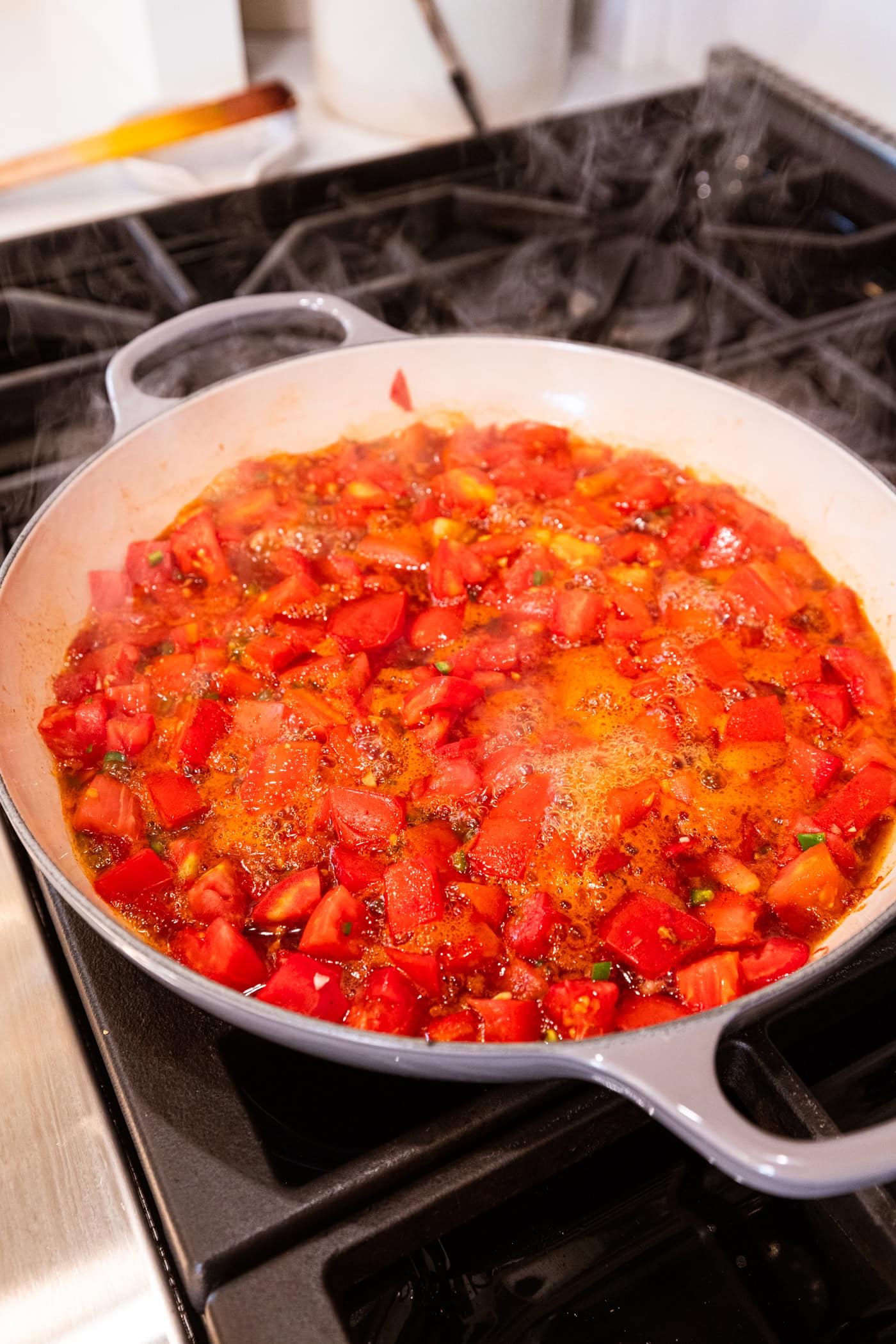 Mixture of chopped tomatoes boiling in a skillet on the stovetop with foam on the top.