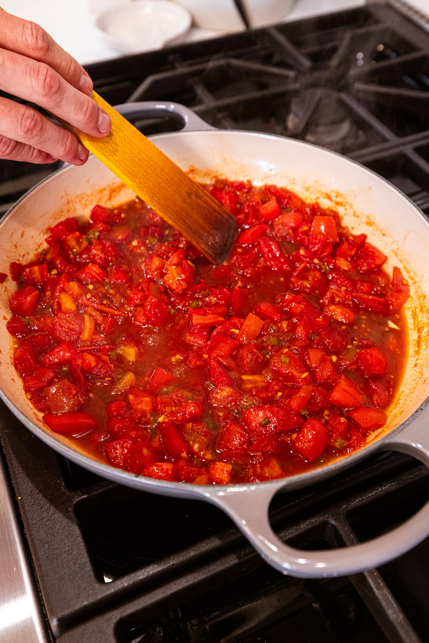 Hand holding wooden spoon mixture together cooking mixture of tomato jam that has a lot of juices coming out.