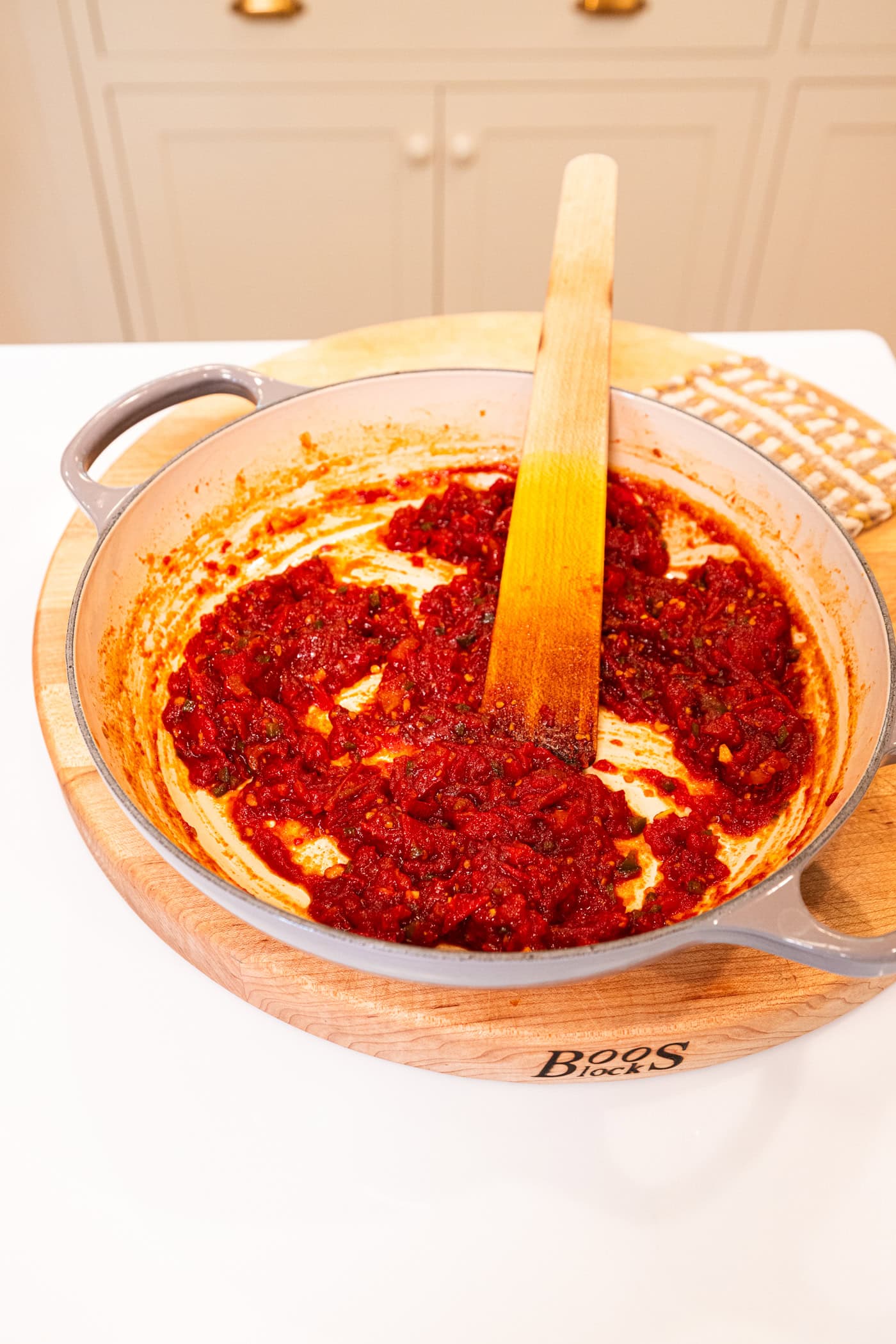 Skillet filled with cooked tomato jam with wooden skillet in pan all on wood cutting board.