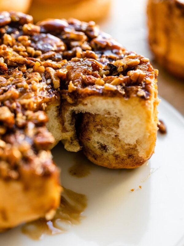 White plate with a circle of sticky buns with caramel topping and nuts on top with two rolls removed.