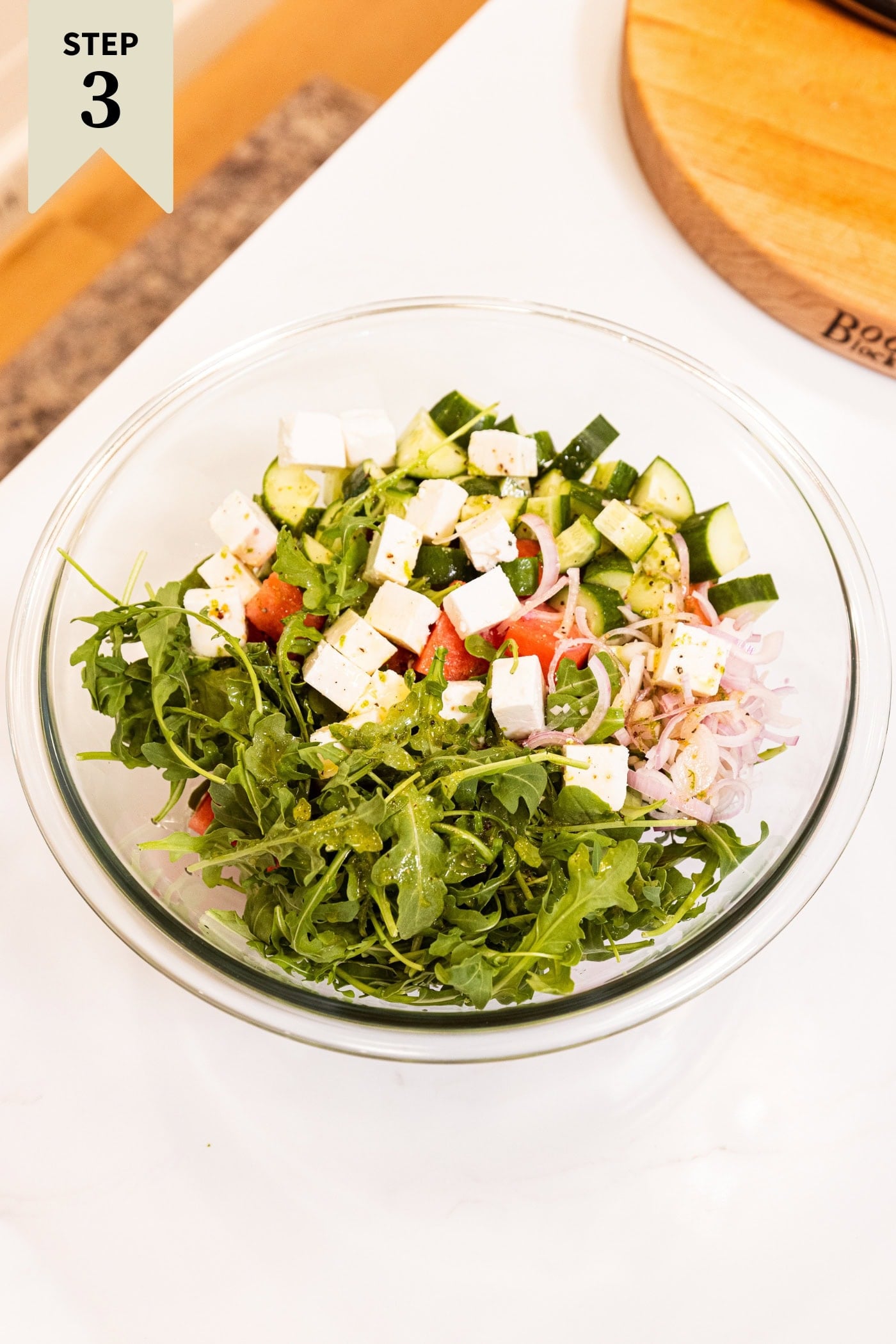 Glass bowl filled with ingredients before being mixed together to form a watermelon salad.