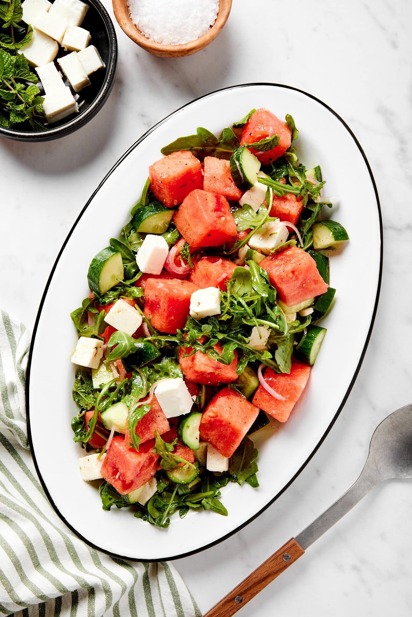 White serving platter with watermelon with feta cheese and arugula showing.