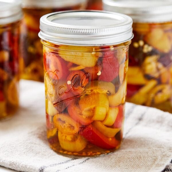 Jar of canned pickled peppers sitting on a towel with more pickle jars to the sides.