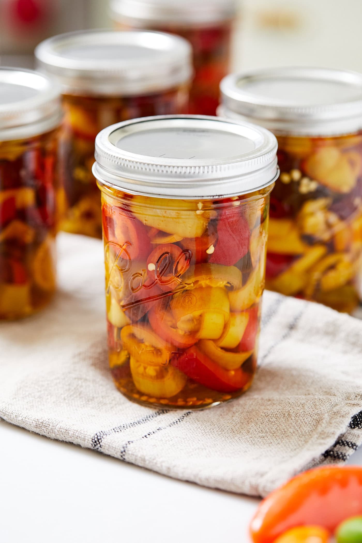 Jar filled with sliced pickled peppers sitting on countertop with more jars around it after being canned in a water bath.