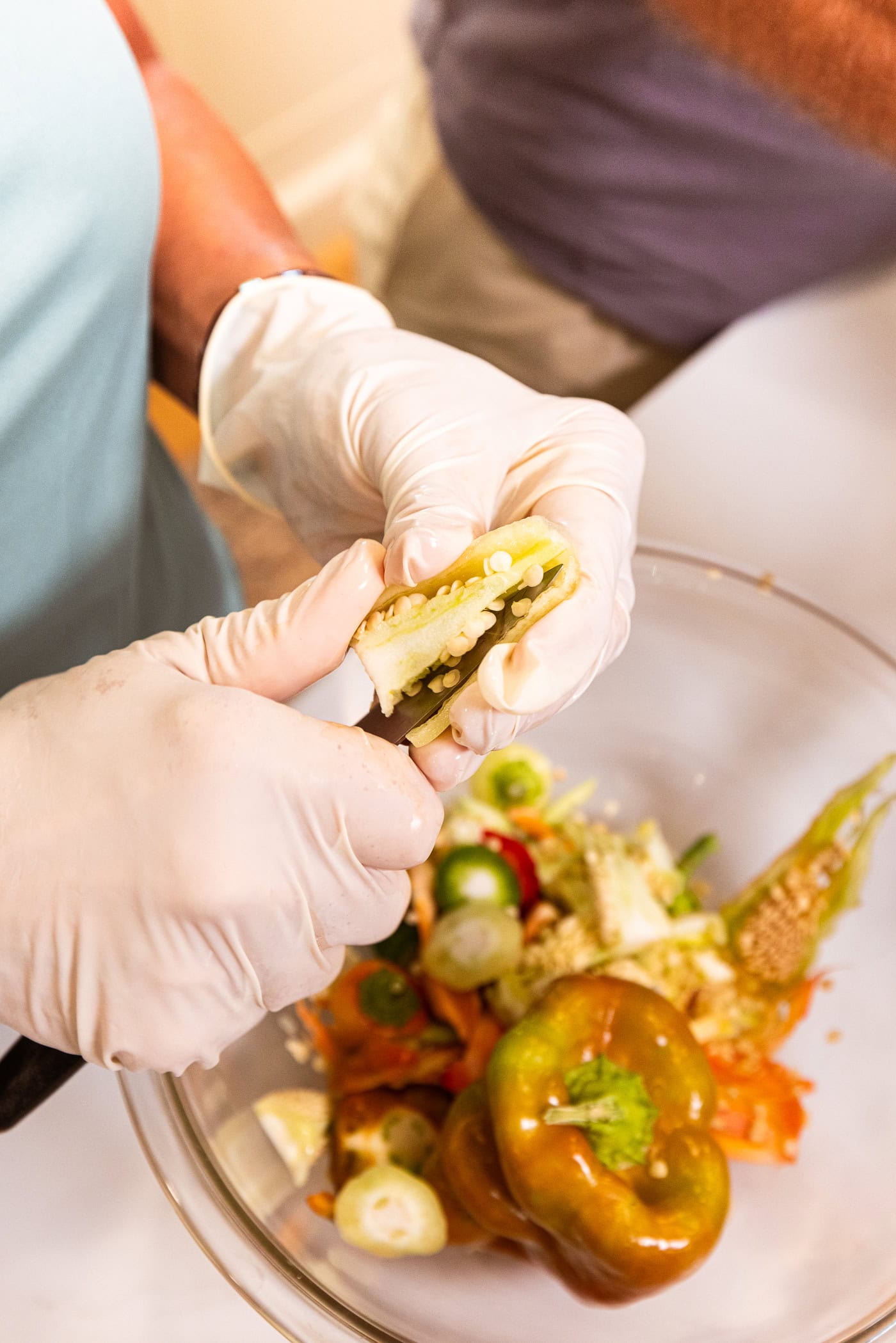 Hands wearing gloves taking the seeds and pith out of the middle of a yellow pepper above a bowl.