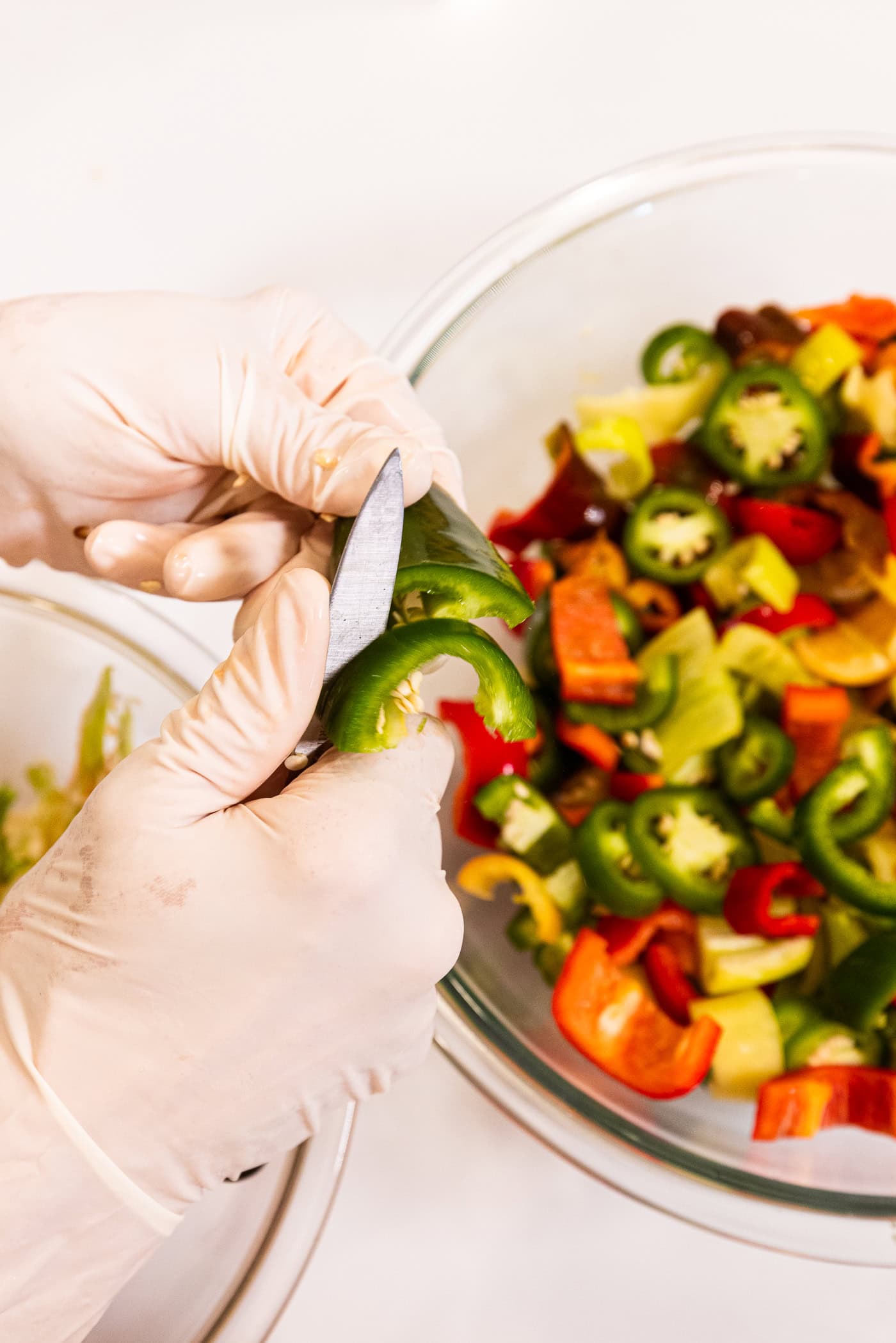 Hands using knife to slice a green pepper into pieces over a bowl filled with more sliced hot peppers.