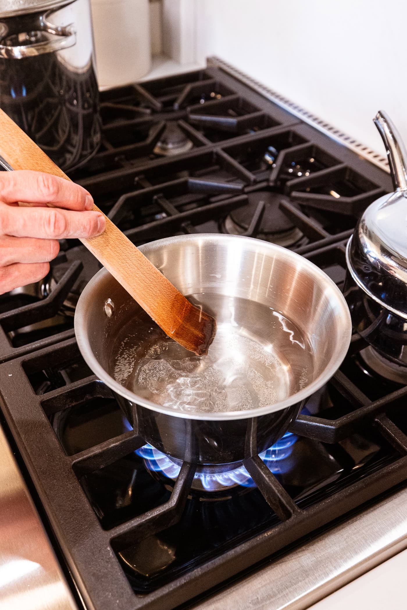 Wooden spatula stirring together a clear brine in a metal saucepan on the stovetop.