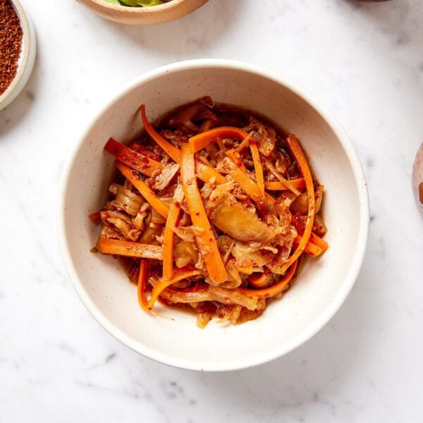 White bowl filled with orange colored kimchi on marble surface.
