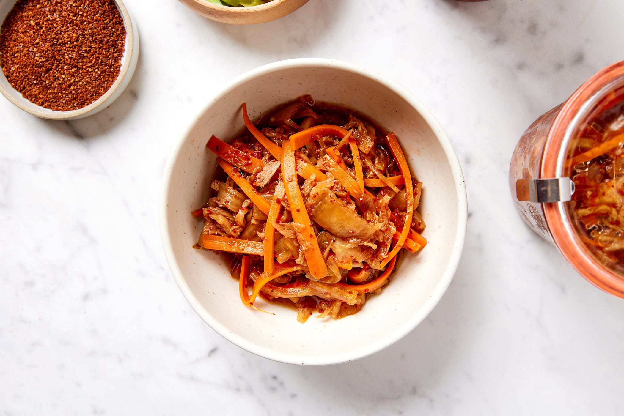 White bowl filled with orange colored kimchi on marble surface.