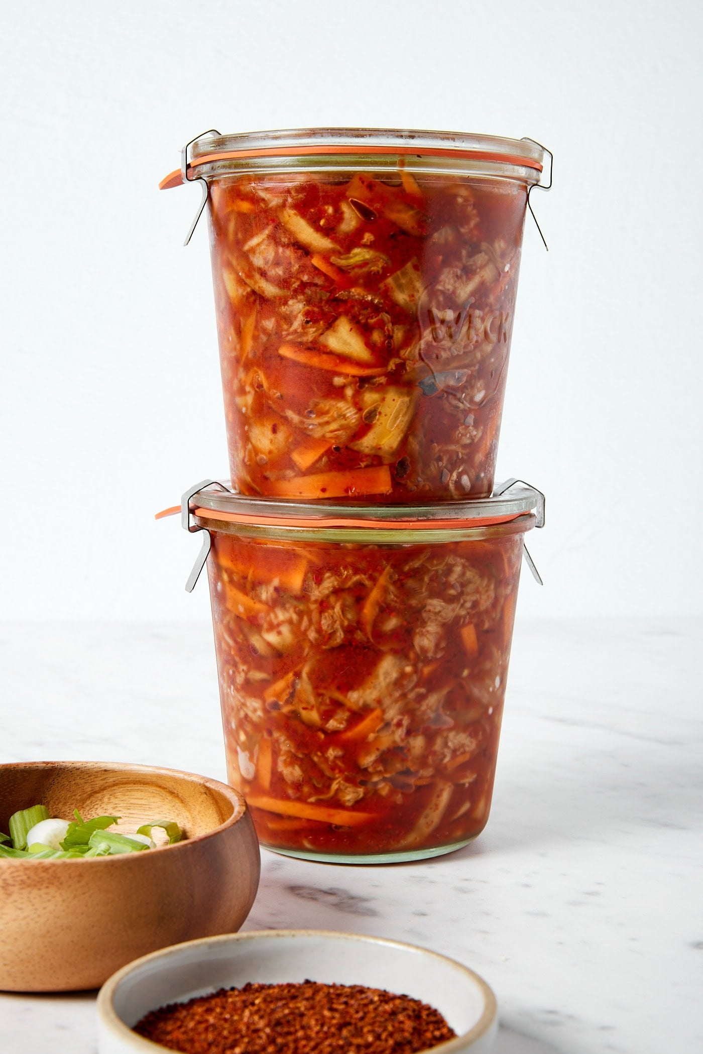 Two glass jars filled with homemade kimchi on a white marble surface showing the fermented orange color inside.