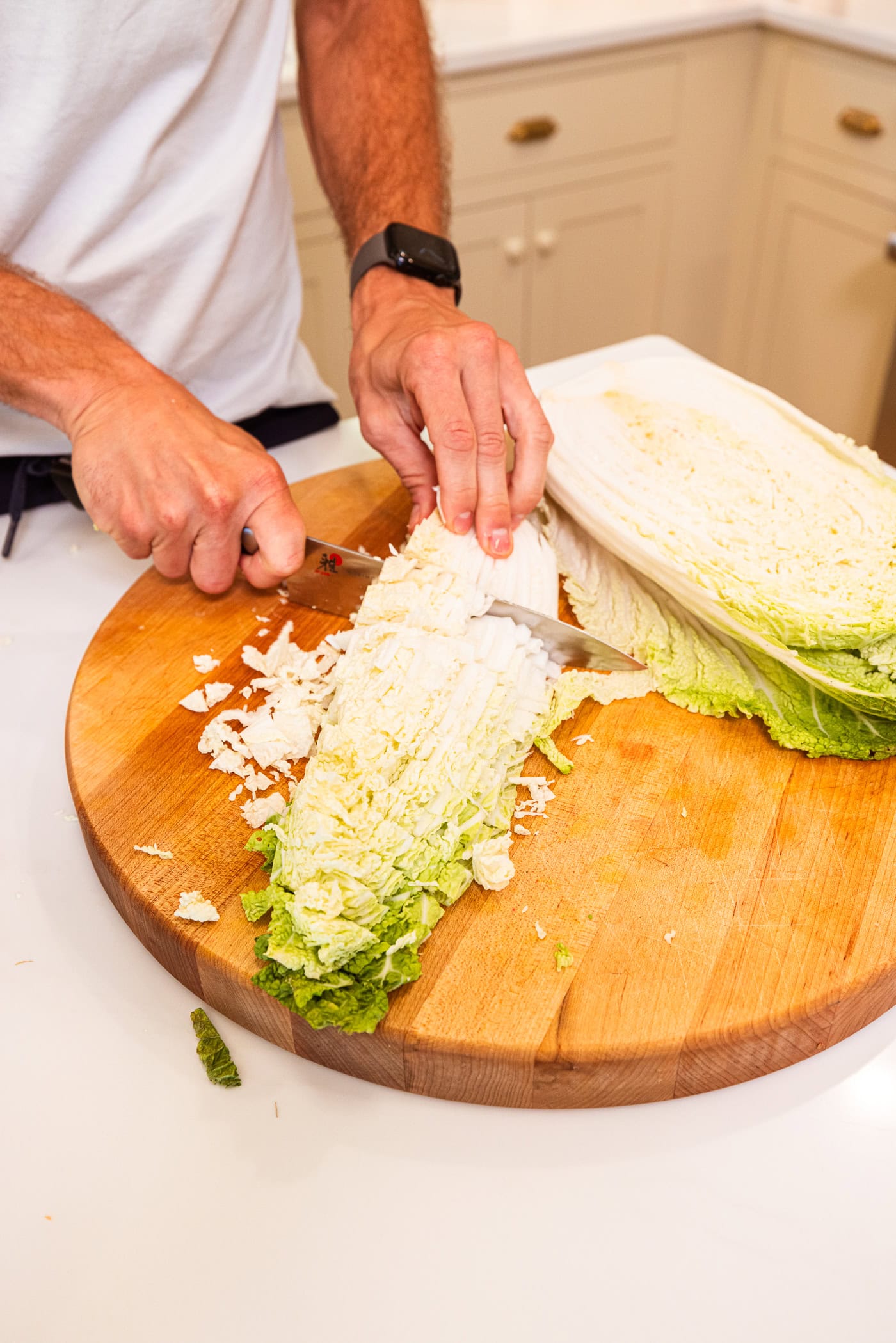 Cabbage being sliced on a wooden cutting board to make homemade kimchi.