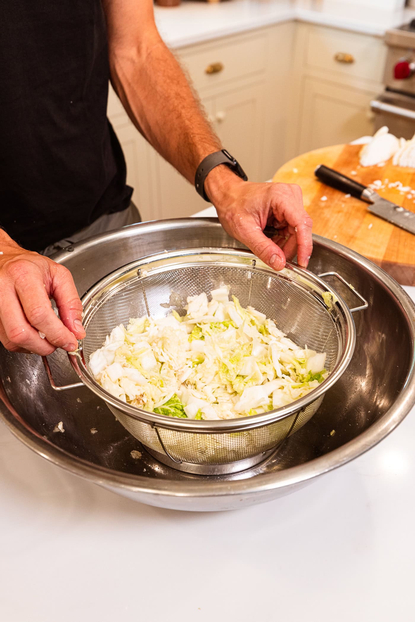 Sliced cabbage in a colander being held over a metal bowl.