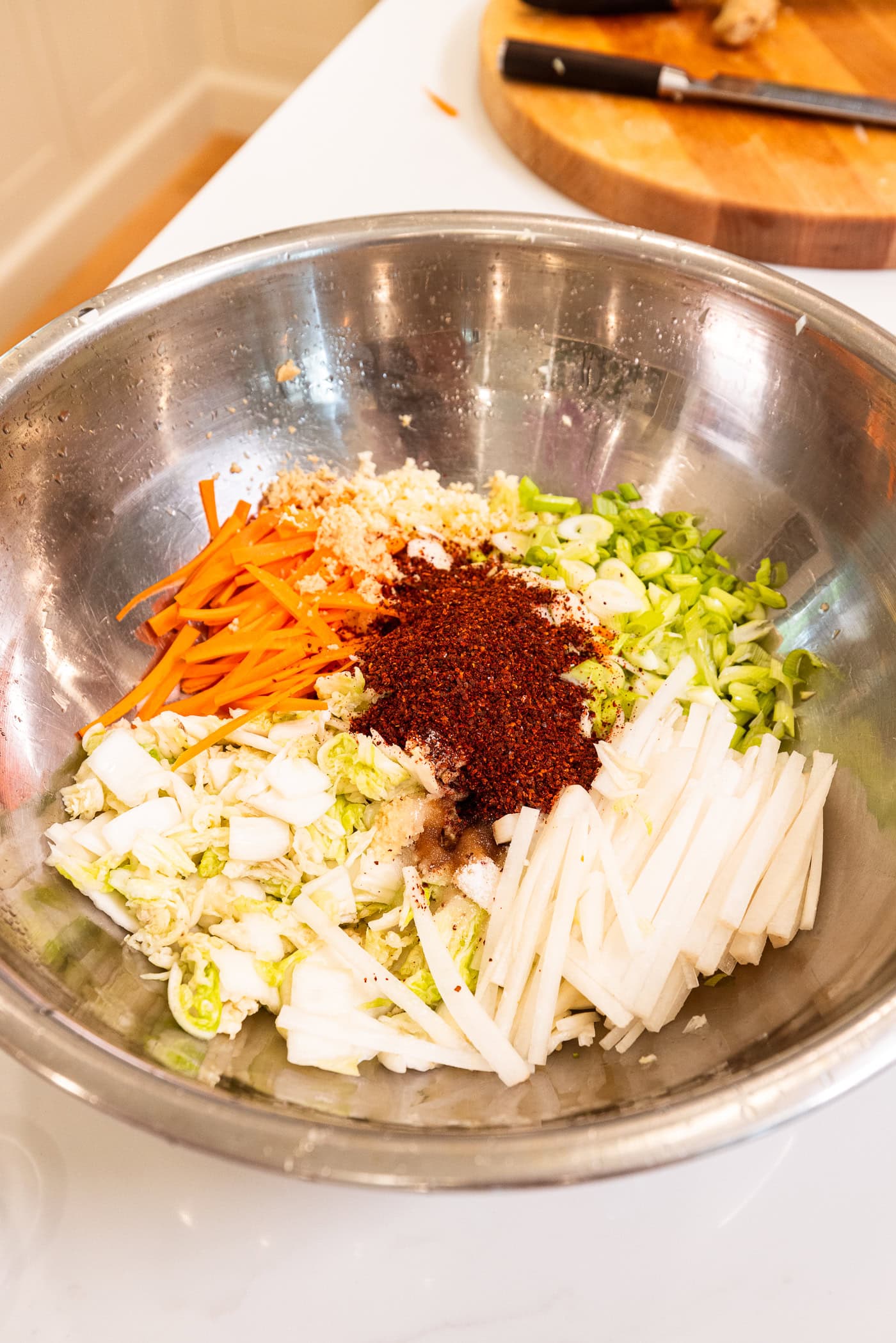 Large metal bowl filled with sliced cabbage and sliced components and spices to make kimchi.