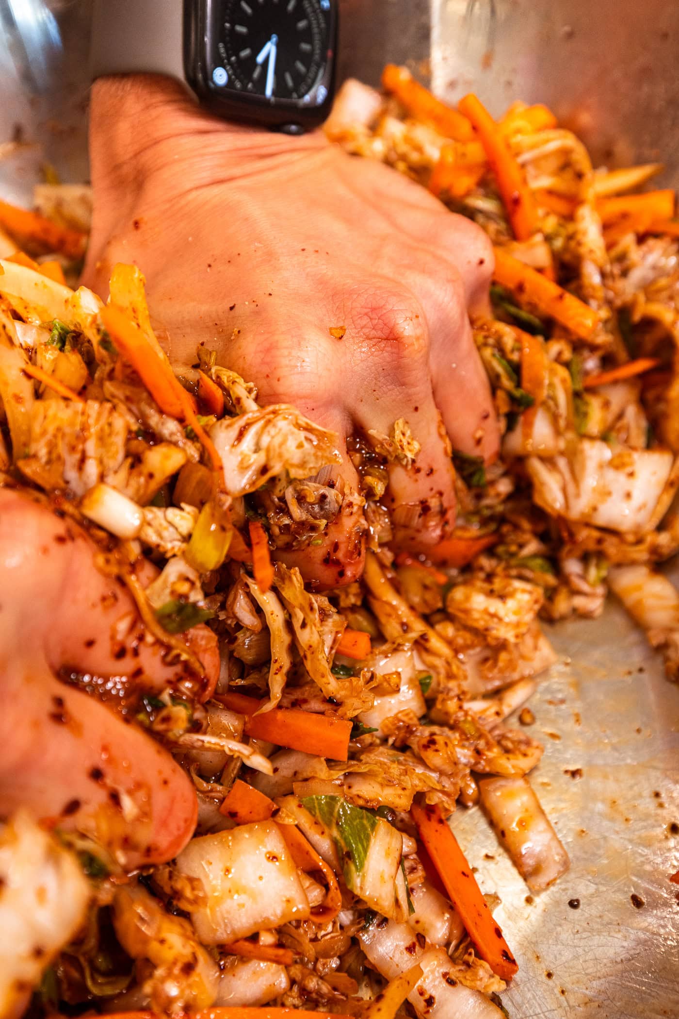 Hand squeezing together shredded cabbage with spices causing an orange color.