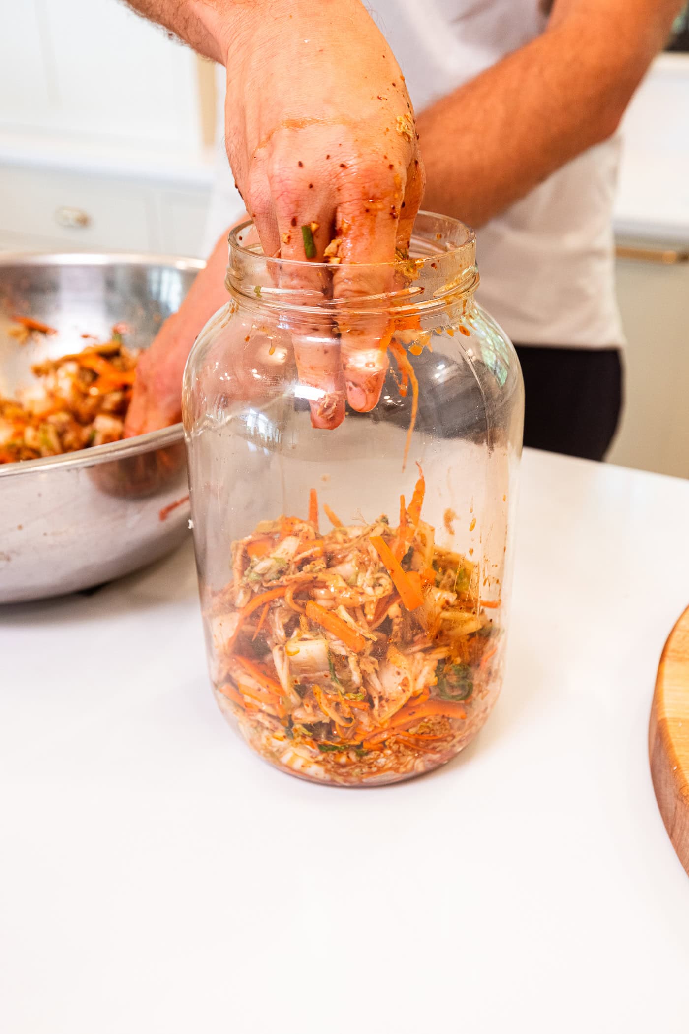 Hand placing pieces of kimchi into a large glass jar to let ferment.