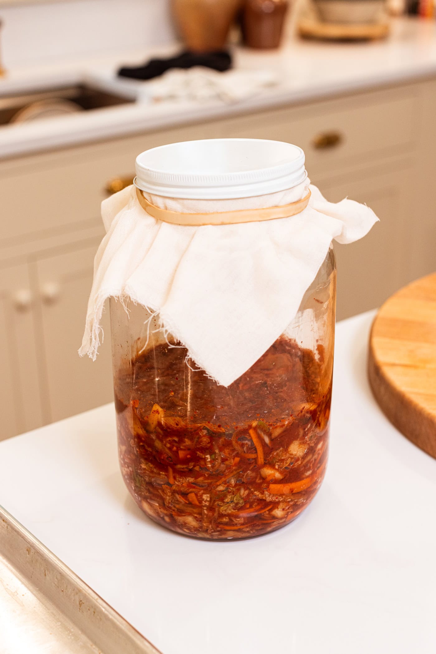 Large glass jar filled with kimchi with cheesecloth over the top with a rubber band securing it in place.