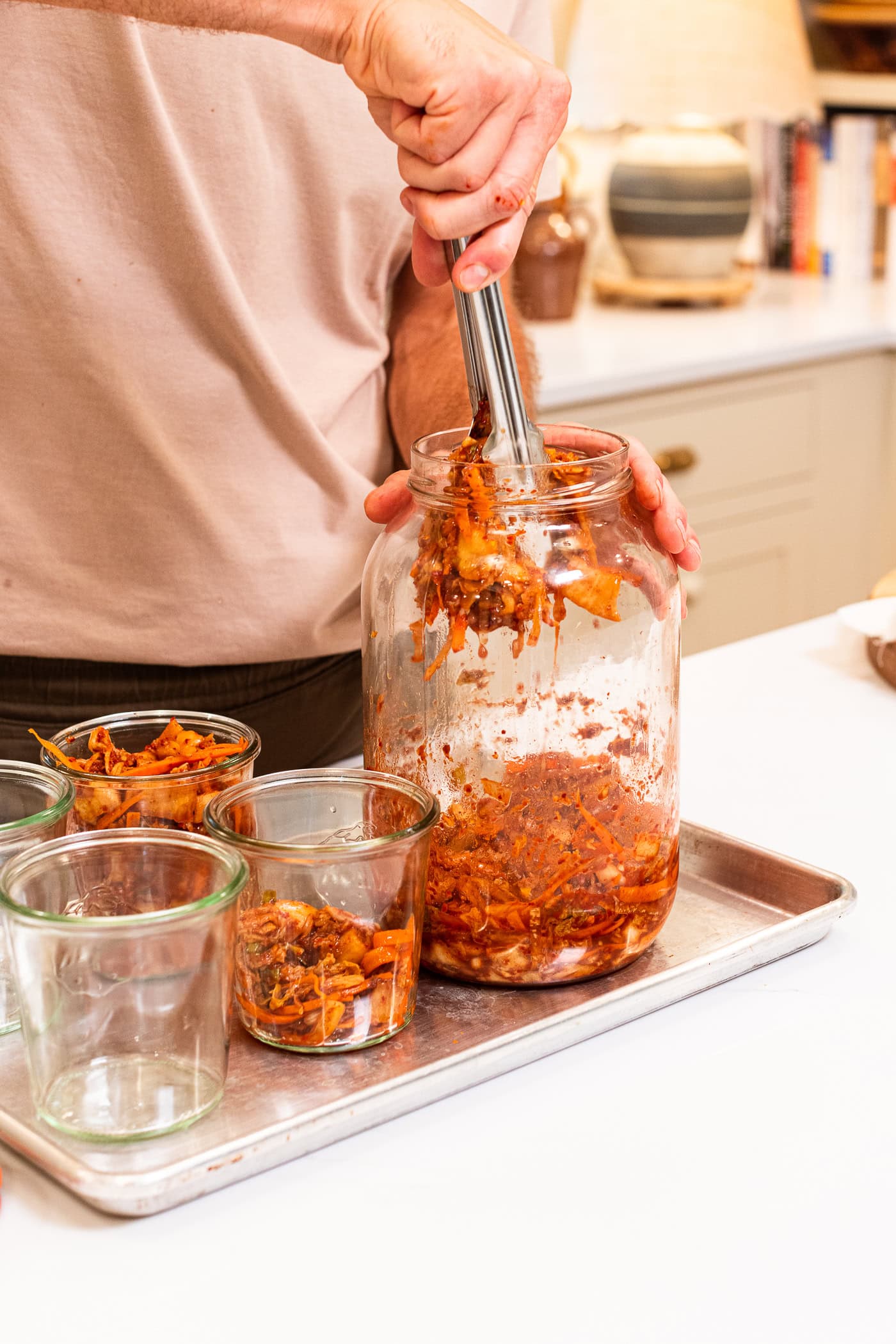 Tongs being used to pull kimchi out of a glass jar to store in smaller glass jars.
