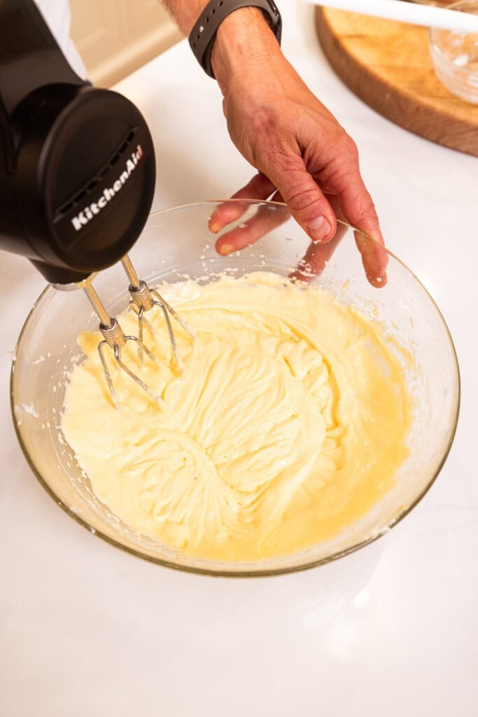 An electric hand mixer beating wet ingredients together to form a batter.