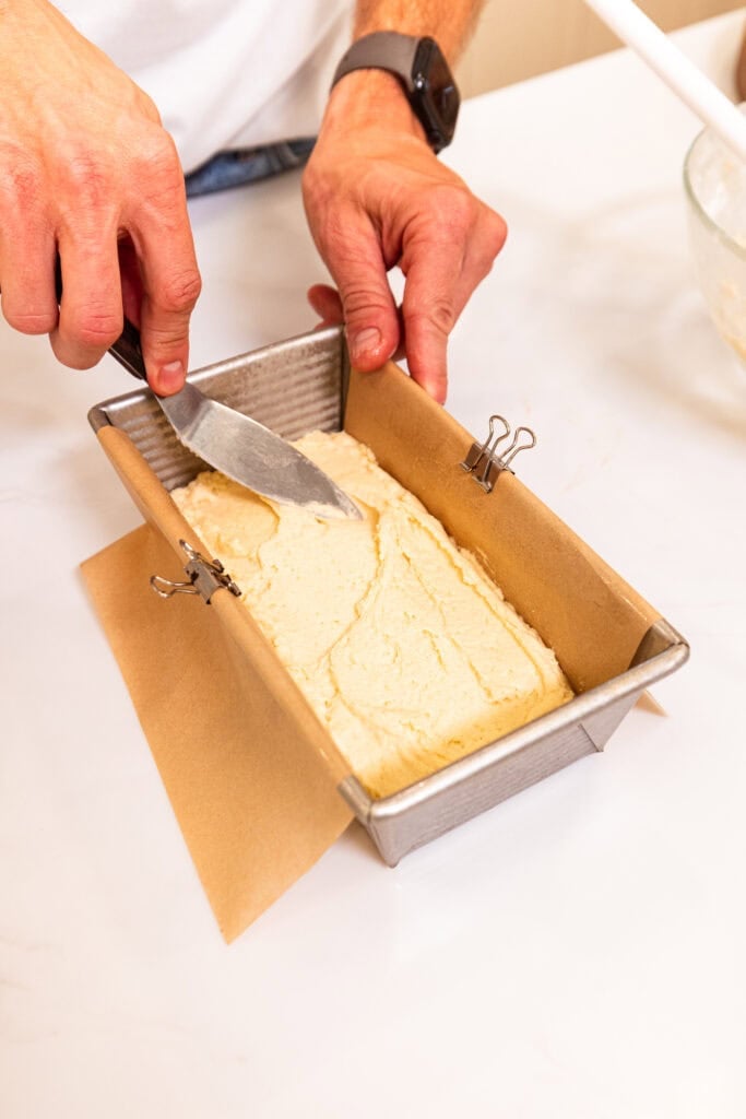 A hand leveling coffee cake batter in a loaf pan.