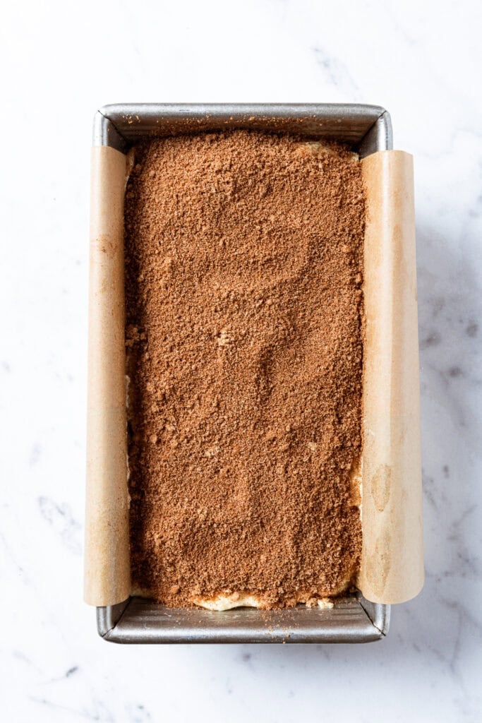 Coffee cake batter topped with a brown sugar crumble sits in a loaf pan before baking.